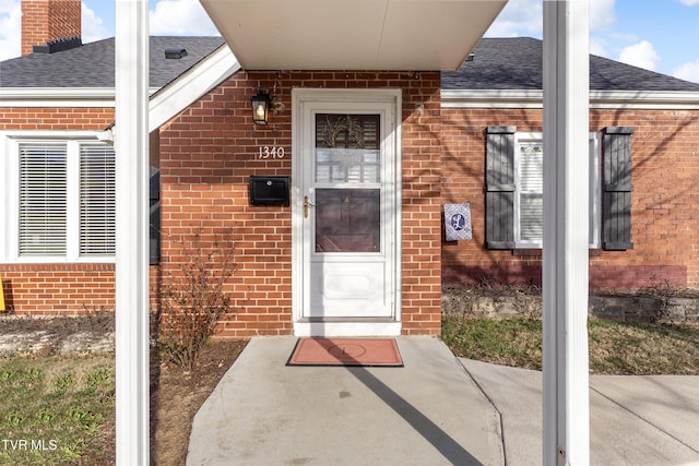 property entrance with a shingled roof and brick siding