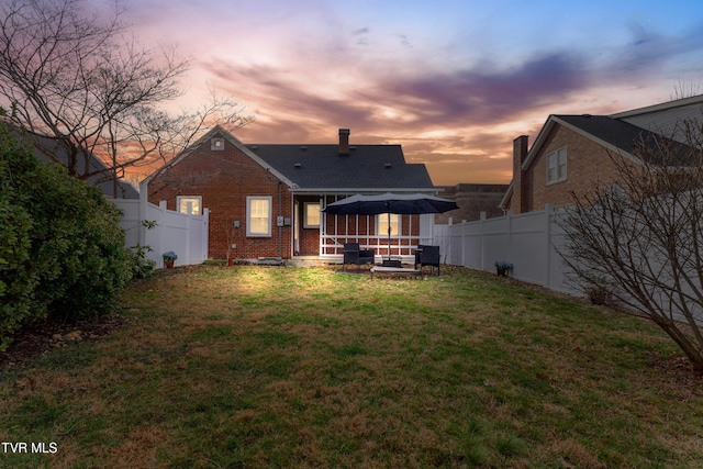 back of house at dusk featuring a yard, brick siding, a gazebo, and a fenced backyard