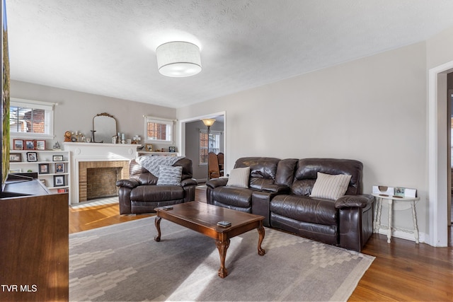 living room with a brick fireplace, a textured ceiling, and wood finished floors