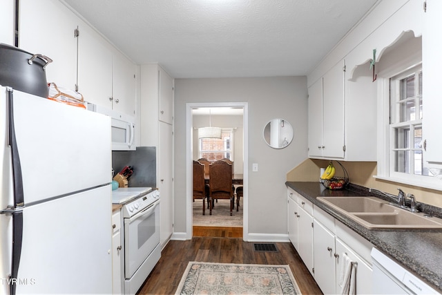 kitchen featuring white appliances, visible vents, white cabinets, dark wood-type flooring, and a sink