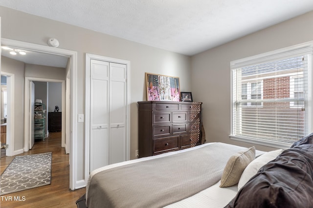 bedroom featuring a closet, a textured ceiling, baseboards, and wood finished floors