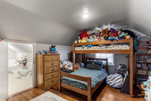 bedroom with lofted ceiling, ensuite bath, and wood finished floors