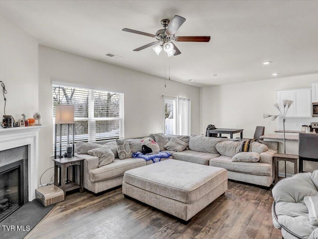 living room featuring dark wood-style floors, recessed lighting, visible vents, a ceiling fan, and a glass covered fireplace