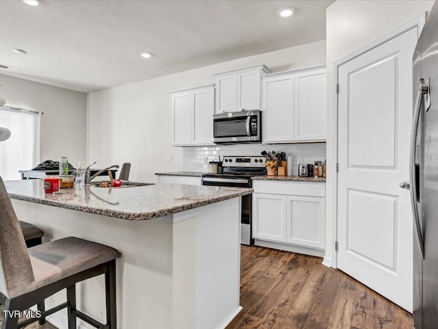 kitchen with white cabinets, appliances with stainless steel finishes, decorative backsplash, dark wood-style floors, and a kitchen bar