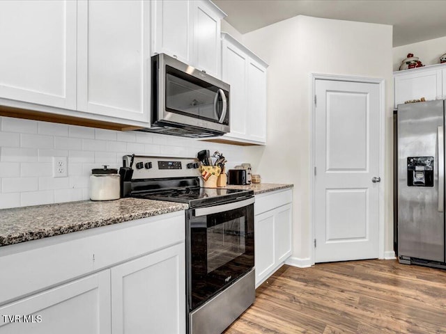 kitchen featuring light wood-style flooring, stainless steel appliances, white cabinets, light stone countertops, and tasteful backsplash