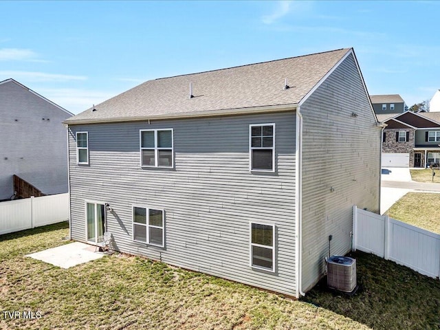 rear view of house with a fenced backyard, central AC, a lawn, and roof with shingles