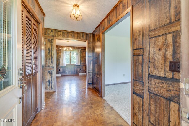 hall with wooden walls, baseboards, a chandelier, and a textured ceiling