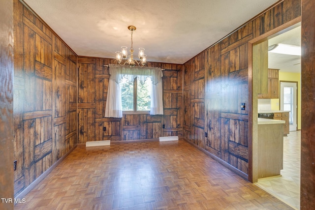 empty room with wood walls, a notable chandelier, baseboards, and a textured ceiling