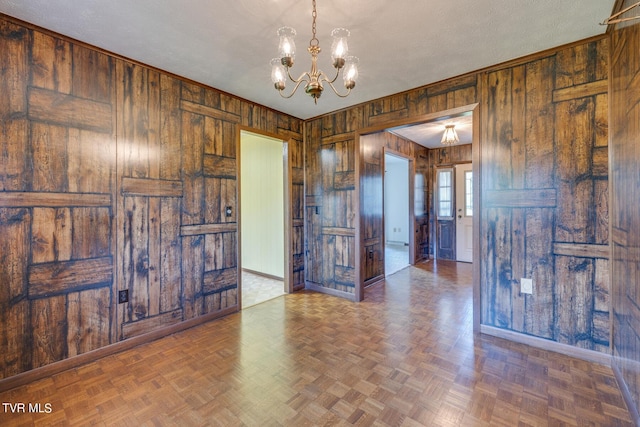 spare room with wood walls, a notable chandelier, baseboards, and a textured ceiling