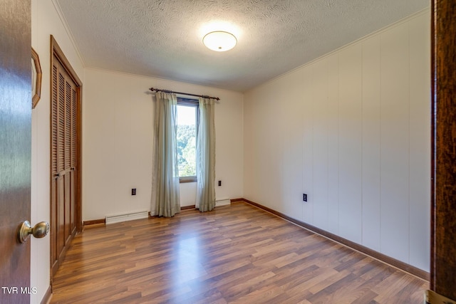 empty room with crown molding, a textured ceiling, baseboard heating, and wood finished floors