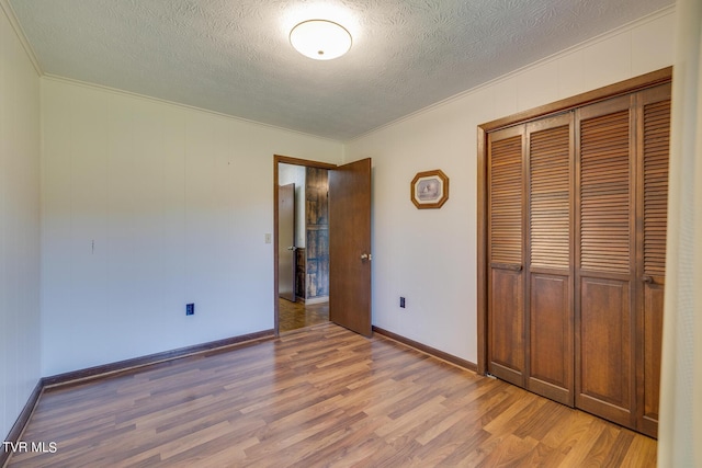 unfurnished bedroom featuring a textured ceiling, baseboards, ornamental molding, a closet, and light wood finished floors