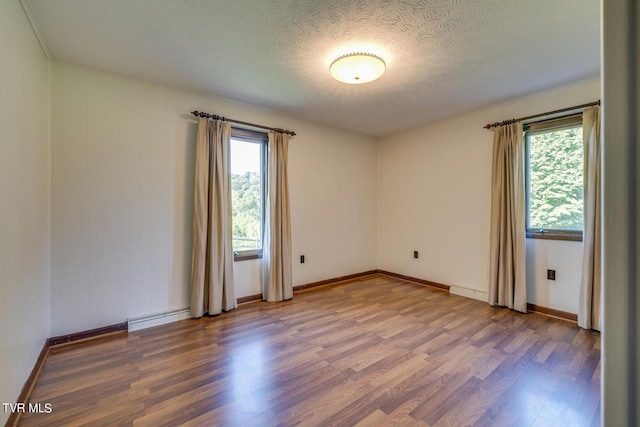 empty room with a baseboard heating unit, a textured ceiling, baseboards, and wood finished floors