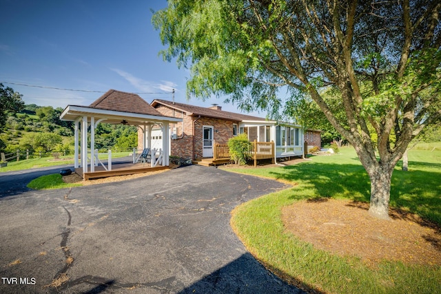 view of front of home featuring a deck, aphalt driveway, brick siding, a front lawn, and a chimney