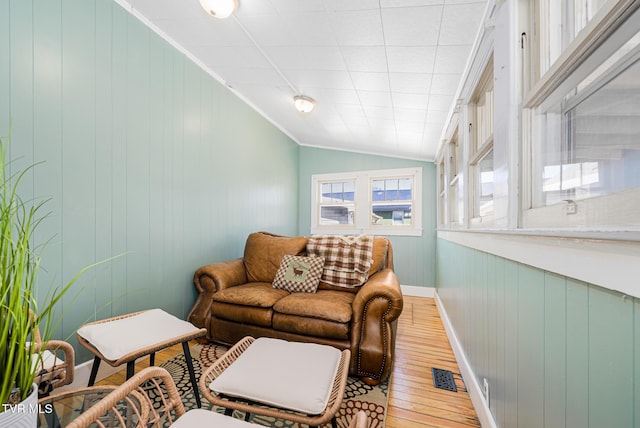 living room featuring visible vents, baseboards, vaulted ceiling, ornamental molding, and light wood finished floors