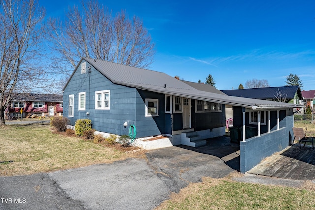 view of front facade featuring entry steps, metal roof, a front lawn, and driveway