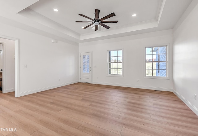 interior space featuring a raised ceiling, baseboards, and light wood finished floors