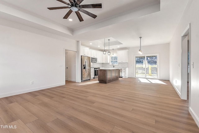 kitchen featuring a raised ceiling, light wood-style flooring, backsplash, appliances with stainless steel finishes, and open floor plan