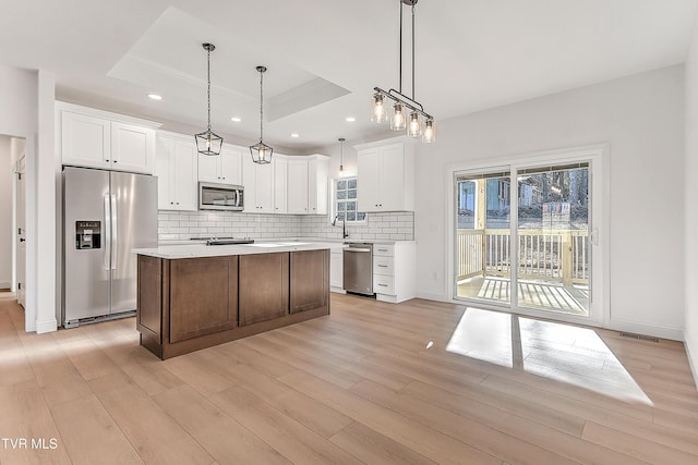 kitchen with a tray ceiling, visible vents, light wood-style flooring, appliances with stainless steel finishes, and a kitchen island