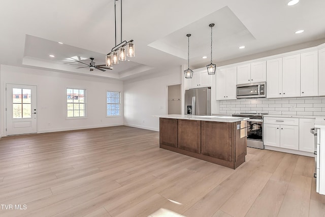 kitchen with a tray ceiling, stainless steel appliances, decorative backsplash, ceiling fan, and a kitchen island