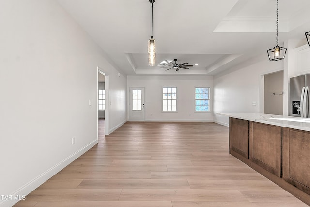 kitchen with a tray ceiling, decorative light fixtures, stainless steel refrigerator with ice dispenser, light wood-style flooring, and a ceiling fan