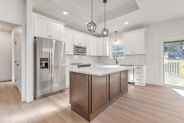 kitchen featuring stainless steel appliances, a raised ceiling, light wood finished floors, and decorative backsplash