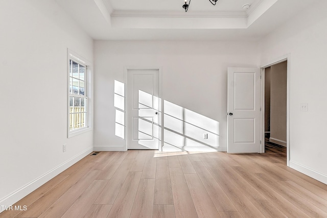 spare room with light wood-style floors, a tray ceiling, crown molding, and baseboards