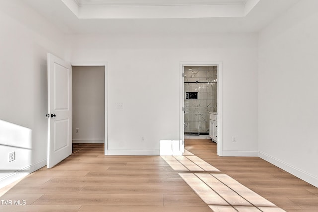 unfurnished bedroom with light wood-type flooring, a tray ceiling, baseboards, and ensuite bathroom