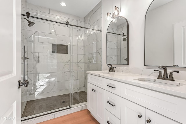 full bathroom with double vanity, a stall shower, a sink, and wood finished floors