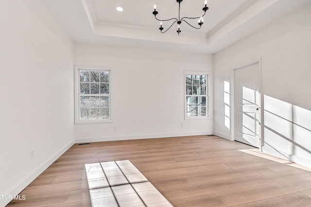 empty room with crown molding, light wood-style floors, a raised ceiling, and an inviting chandelier