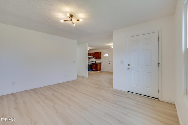 empty room with light wood-style floors, baseboards, and a textured ceiling