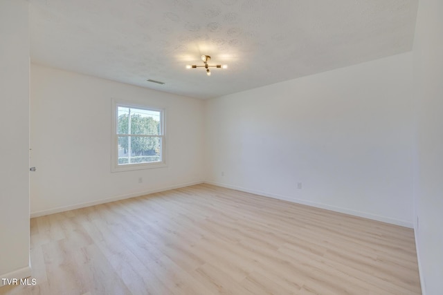 unfurnished room with a textured ceiling, light wood-style floors, visible vents, and baseboards