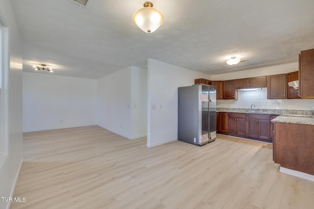 kitchen featuring light wood-style flooring, freestanding refrigerator, a sink, a textured ceiling, and tasteful backsplash