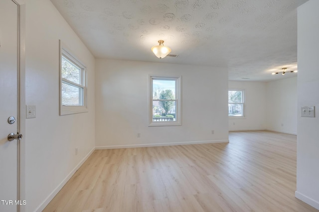 spare room with baseboards, a textured ceiling, and light wood-style flooring