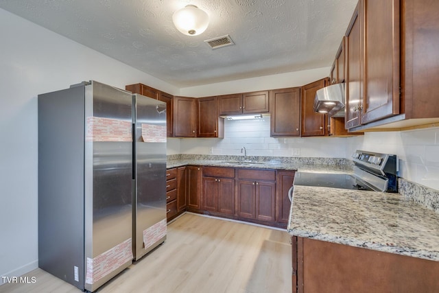 kitchen featuring light wood finished floors, extractor fan, light stone counters, appliances with stainless steel finishes, and a sink