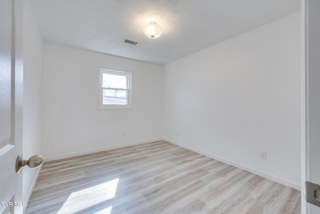 spare room featuring light wood-type flooring, visible vents, and baseboards