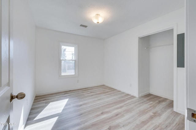 unfurnished bedroom featuring visible vents, baseboards, electric panel, light wood-style floors, and a closet