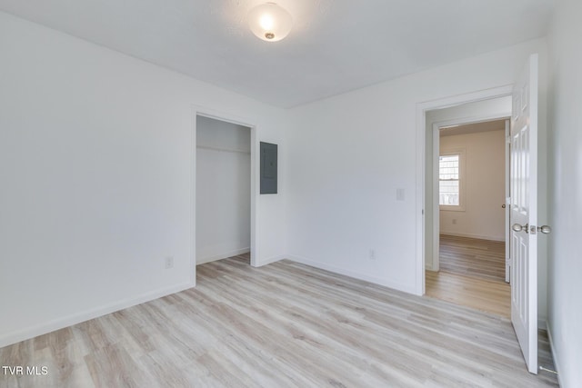 unfurnished bedroom featuring electric panel, baseboards, light wood-type flooring, and a closet