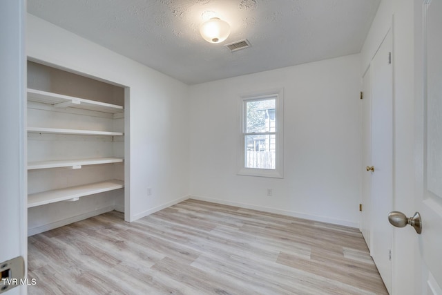 unfurnished bedroom featuring visible vents, a textured ceiling, a closet, light wood-style floors, and baseboards