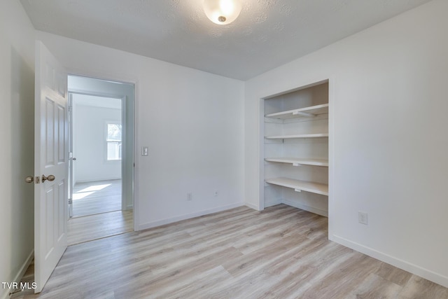 unfurnished bedroom with a closet, baseboards, a textured ceiling, and light wood finished floors