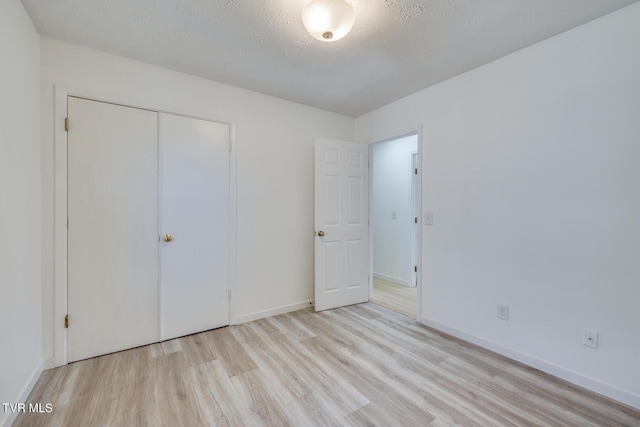 unfurnished bedroom with a closet, a textured ceiling, baseboards, and wood finished floors