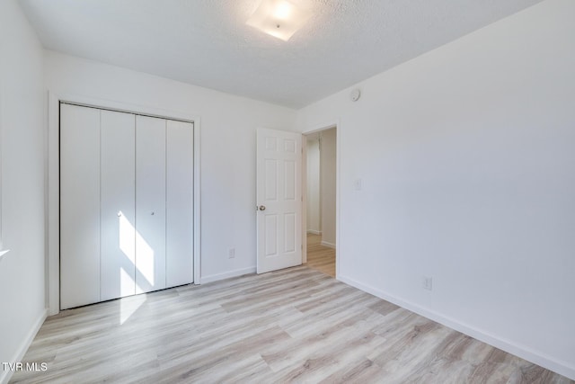 unfurnished bedroom featuring a closet, a textured ceiling, baseboards, and wood finished floors