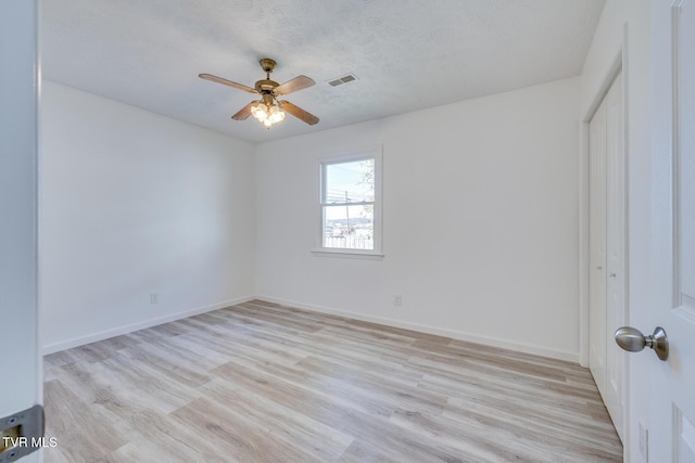 unfurnished room featuring baseboards, visible vents, a textured ceiling, and light wood-style floors