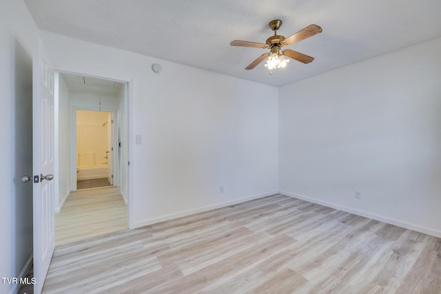 unfurnished room featuring light wood-type flooring, baseboards, attic access, and ceiling fan