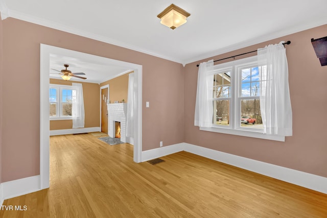 spare room featuring a fireplace, baseboards, light wood-style floors, and ornamental molding