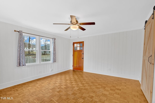 unfurnished room with a barn door, baseboards, ceiling fan, and crown molding