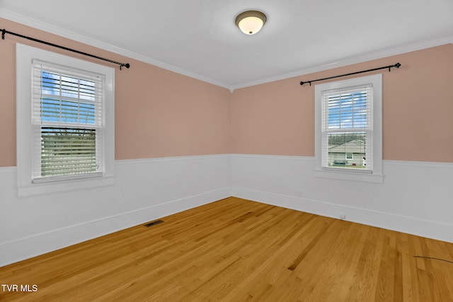 empty room with a wainscoted wall, crown molding, and light wood finished floors