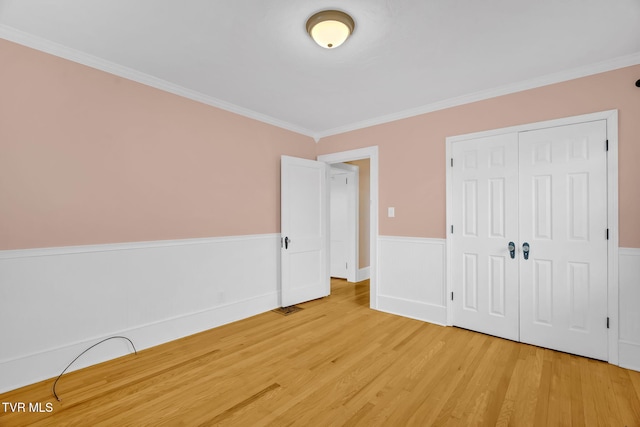 unfurnished bedroom with light wood finished floors, a wainscoted wall, crown molding, and a closet