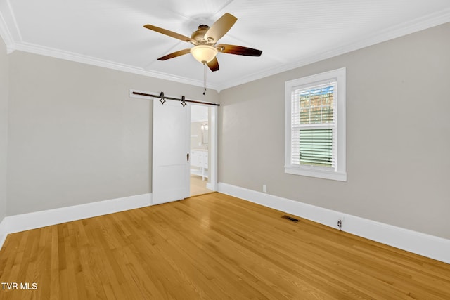 spare room featuring visible vents, a barn door, crown molding, light wood finished floors, and baseboards