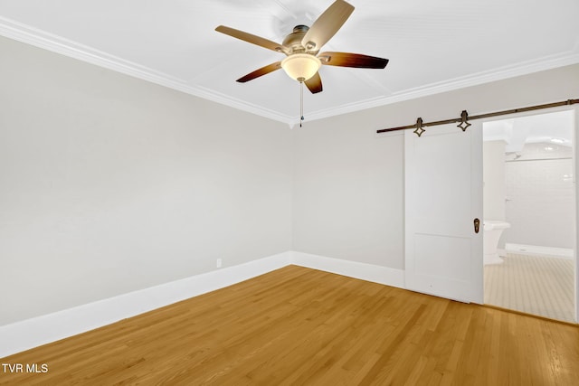 empty room featuring ceiling fan, baseboards, a barn door, ornamental molding, and light wood-style flooring