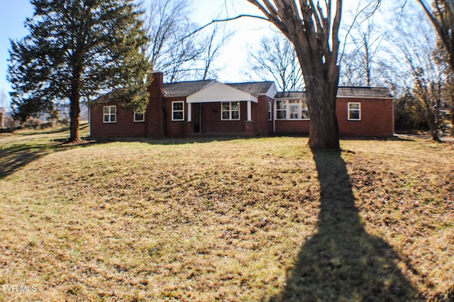 view of front facade with brick siding, a chimney, and a front yard